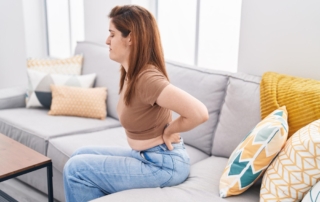 Woman sitting on a couch holding her lower back due to pain and discomfort at home