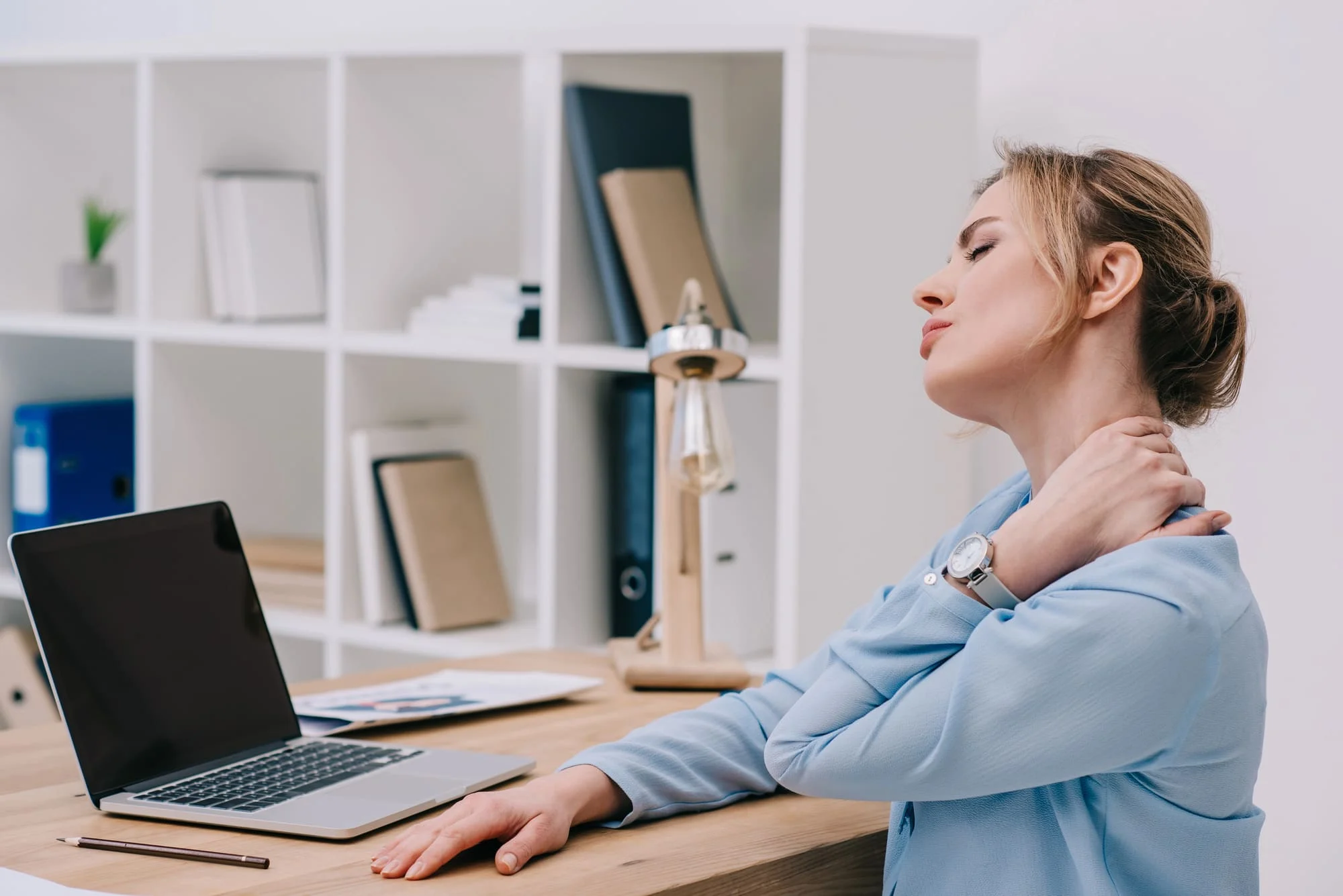 Woman at her desk holding her neck in pain while working